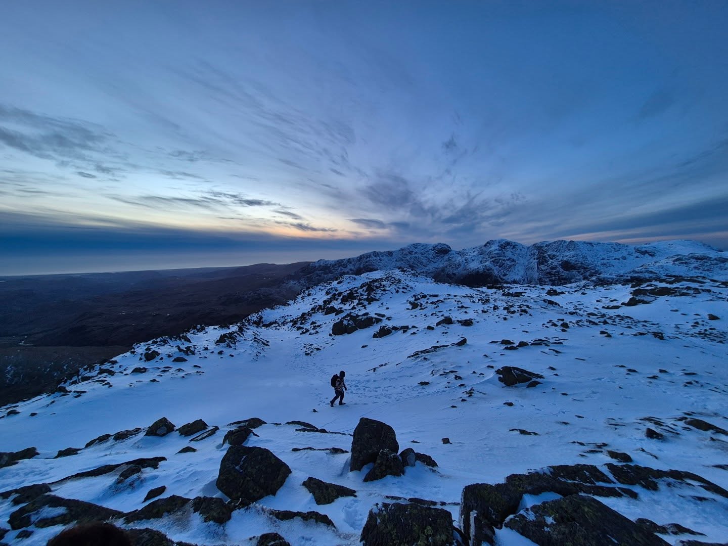 Solo hiker crossing a snowy mountain summit at sunset — the Lakeland terrain Dark Peak instructors are qualified to work on